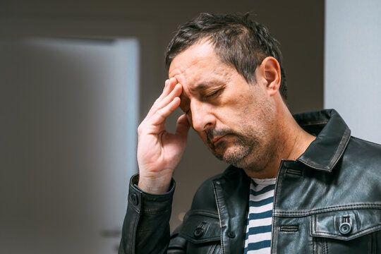 Confused adult male in leather jacket tapping his forehead, searching his memory in a moment of recall effort.