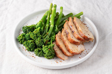 Minimalist healthy meal with green broccolini and roasted turkey breast served on a white plate on a linen tablecloth