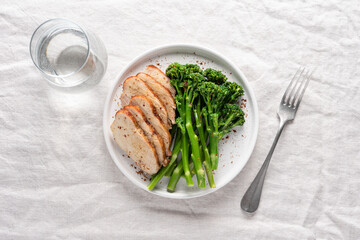Minimalist healthy meal with green broccolini and roasted turkey breast served on a white plate on a linen tablecloth