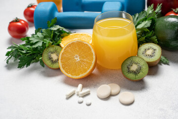 Youth and Health Preservation Concept with Vitamins, Dumbbells, Fresh Vegetables, Fruits, Greens and Orange Juice on Light Background