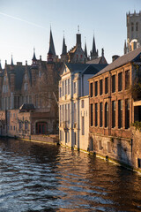 Golden hour Bruges canal with historic brick houses and gothic spires reflected in water, medieval old town cityscape in Belgium