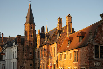 Golden hour view of historic brick buildings and church tower in Bruges old town, Belgium, warm evening light on medieval Flemish architecture