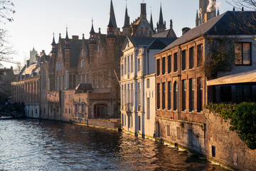 Golden hour view of Bruges canal with medieval brick buildings and gothic spires reflecting in shimmering water under clear winter sky