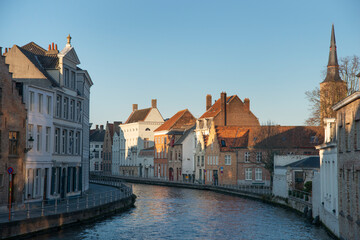 Picturesque European canal in Bruges with historic brick townhouses, white facades and church spire in warm evening light, tranquil waterway curving through old city.jpg