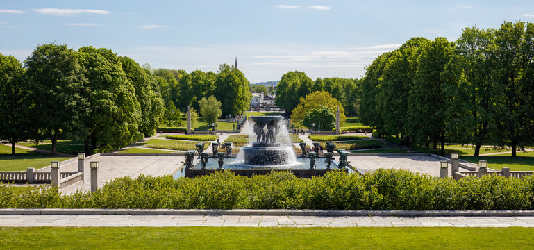 Busy city quiet moment in Frognerpark with fountain surrounded by lush greenery, pathways and serene landscape during a sunny day