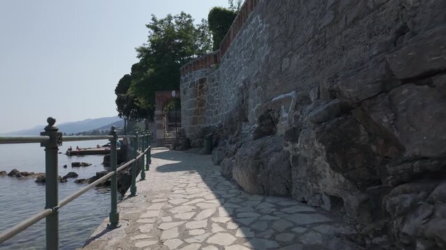 
Walking along the Lungomare Coastal Promenade in Volosko, Croatia on a sunny summer day. Rocky Adriatic Sea coastline with railings and blue water. The famous seaside walkway is over 100 years old.