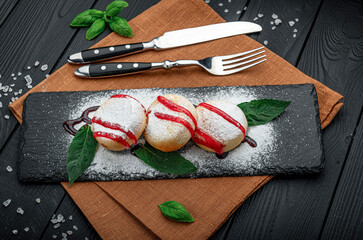 Fresh dessert served on slate plate with cutlery and garnish. Three round desserts are on a dark...