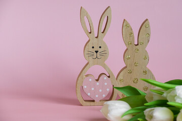 Obraz premium Wooden Easter bunnies on a delicate pink background with white tulips. Theres room for text.