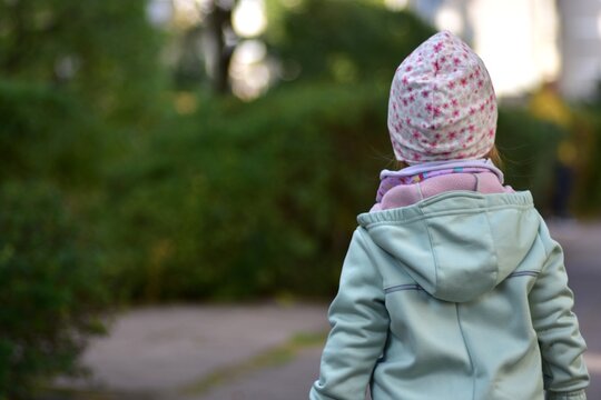 Small toddler walking alone on a sidewalk in a green residential area, photographed from behind. Childhood independence, early exploration, outdoor activity and calm everyday life moment in the city.