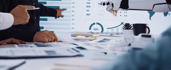 A collaborative meeting scene showcasing human hands and a robotic arm interacting with visual data, symbolizing the fusion of technology and teamwork in business analysis.Noogenesis