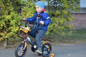 Fototapeta premium Toddler riding a small bicycle with training wheels along a park path. Active childhood, learning balance, outdoor play and healthy lifestyle concept with motion and natural surroundings.