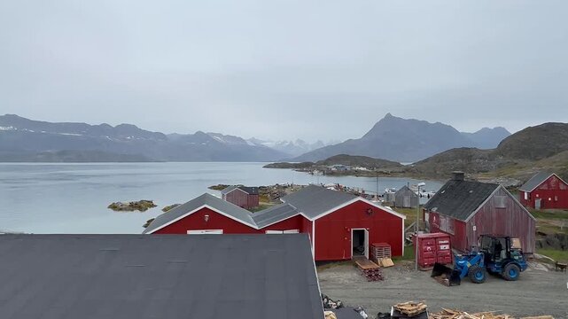 A scenic view of Tasiilaq village nestled among towering mountains in eastern Greenland. Colorful houses contrast with rugged rocky peaks and the vast Arctic landscape