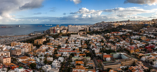 Aerial view shows Las Palmas de Gran Canaria, grid homes to high rise core, Atlantic port with marinas and ships, beachfront avenue and breakwater in late afternoon light. © Aerial Film Studio