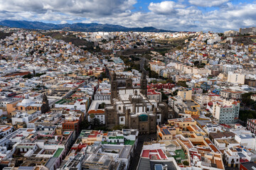 Fototapeta premium Aerial daytime view of Las Palmas de Gran Canaria, Catedral de Santa Ana at center, narrow streets and low rise buildings in Vegueta, soft light, clouds, volcanic hills.