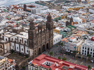 Aerial view shows Catedral de Santa Ana with twin towers and rose window, Vegueta, Las Palmas de Gran Canaria, pedestrians in plaza, Atlantic on horizon, daytime. © Aerial Film Studio