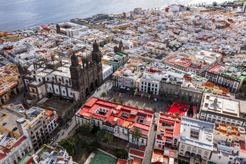 Aerial view shows the Cathedral of Santa Ana, Plaza de Santa Ana, and a Christmas market in Las Palmas de Gran Canaria, with Atlantic shoreline and Vegueta district. © Aerial Film Studio