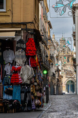 A vibrant narrow street in Granada, Spain, featuring shops with traditional flamenco dresses and souvenirs leading toward a historic cathedral dome.