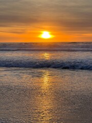 Obraz premium A beautiful sunset over the ocean, casting a golden glow on the water. The waves gently touch the shore, creating a peaceful and serene beach scene.