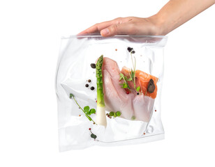 Fresh food, chicken, salmon, and asparagus vacuum sealed in a clear bag, hand holding it