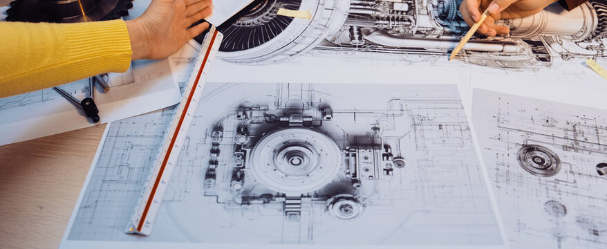 This image captures a collaborative engineering session where hands engage with technical drawings and mechanical components, illustrating teamwork and innovation in design processes. SACTR
