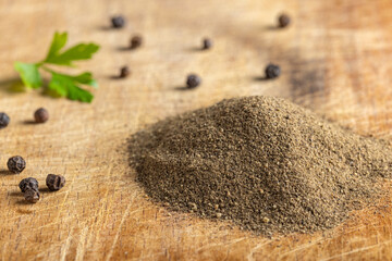 Freshly ground black pepper with whole peppercorns and parsley leaf on wooden board.