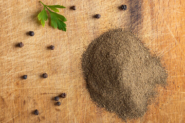 Freshly ground black pepper with whole peppercorns and parsley leaf on wooden board.
