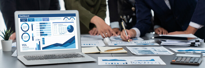 Panorama shot analyst team utilizing BI Fintech to analyze financial report with laptop. Businesspeople analyzing BI data dashboard displayed on laptop screen for business insight. Prodigy