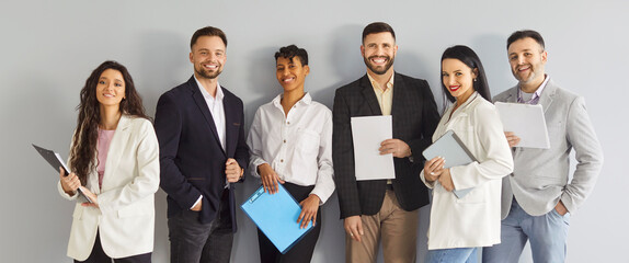 Group of happy diverse business people being friendly colleagues, wearing formal clothes, posing against white wall and holding clipboards, working as team, demonstrating unity support at work