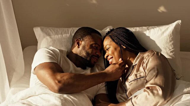 Romantic african american couple cuddling in bed during a beautiful sunny morning. Happy adult man and woman showing affection and intimacy in a comfortable home bedroom