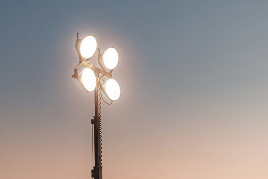 Mobile light tower with bright spotlights against sunset sky. Portable construction lighting equipment for night work.
