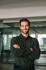 Fototapeta premium Handsome latin hispanic young business man with crossed arms smiling at camera. European confident mature good looking middle-aged leader male businessman on blur office background. Vertical portrait
