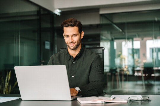 Happy latin hispanic young business man working on laptop computer in company office. Smiling European entrepreneur manager businessman using pc for communication, learning at workplace. Copy space