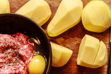 Raw minced meat, peeled yellow potatoes and egg on wooden board. Ingredients for stuffed potato...