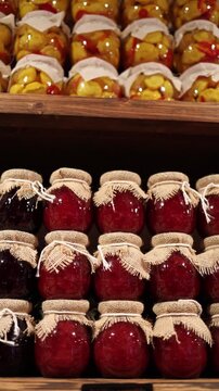 Vertical screen rows of glass jars with preserved vegetables and fruit in grocery store shelves rustic food display homemade pickles jams tradition local harvest