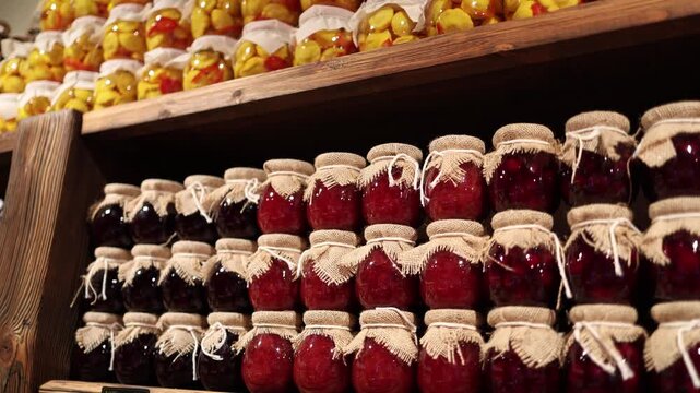 Rows of homemade fruit preserves fill wooden shelves creating a cozy market atmosphere with glass jars fabric lids rich colors and traditional food storage mood