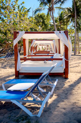 White cabana and lounge chairs on sandy beach facing the ocean in the Dominican Republic, surrounded by palm trees under clear blue skies.
