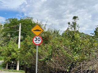 Placa de sinaliza&ccedil;&atilde;o de transito com seta amarela e radares fixo no poste com fundo desfocado a natureza selvagem.