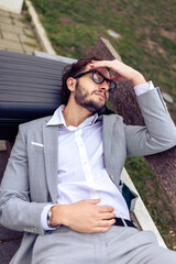 Young businessman resting on a bench in a park with his eyes closed