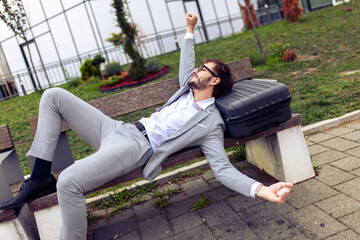 Young businessman resting on a bench in a park with his eyes closed