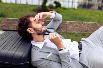 Young businessman resting on a bench in a park with his eyes closed