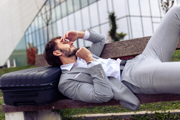 Young businessman resting on a bench in a park with his eyes closed