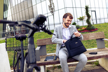 Young businessman placing his tablet into a bag while standing in a city environment with a bicycle.