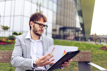 Young Businessman Reviewing Paper Documents on Bench