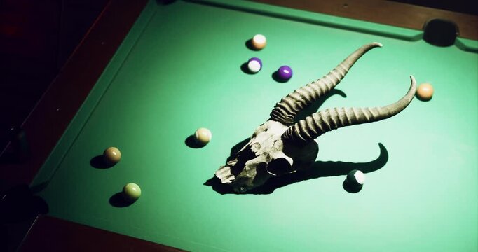 A striking display on a green felt pool table shows a skull with impressive horns at its center, surrounded by colorful billiard balls. The dim lighting adds an intriguing atmosphere.