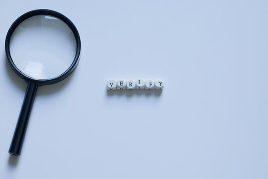 Clean concept image of the word &ldquo;verify&rdquo; with a magnifying glass on a white background, symbolizing fact-checking and accuracy.