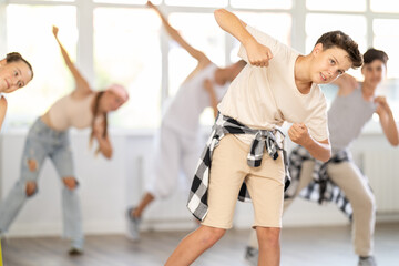 Obraz premium Teen guy together with group of teen friends, learn to dance hip hop in choreo hall. Team of dancers performs sequence of steps combination hand movements, energetic hobby leisure activity of youth