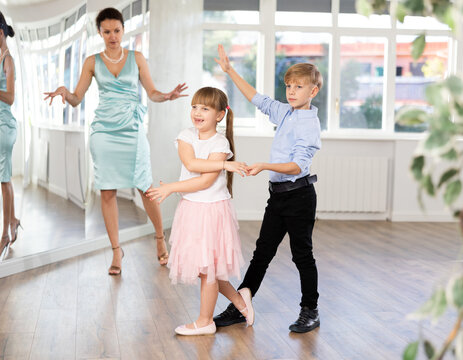 Boy paired up with girl during ballroom dancing lesson. Children rehearse waltz while female teacher conduct dance class