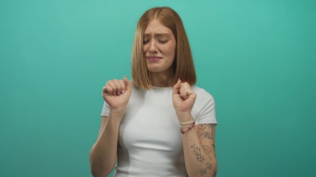 Young woman wrinkles nose and raises hands in studio with green wall; disgust repulsion aversion rejection.