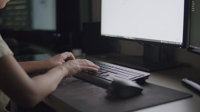 Person typing on keyboard in front of computer monitors in a dark room