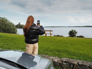 Stylish girl in black jacket and light brown pants is standing by a car, wonderful nature scene...